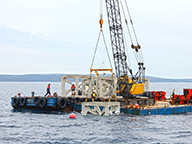 An artificial reef structure being lowered into the ocean from a barge.